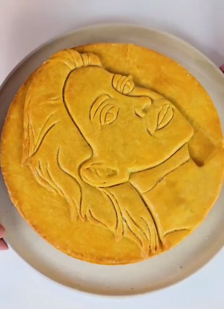 A massa do empadão da imagem anterior foi coberta com um disco de massa assada perfeitamente dourada com o rosto da Fernanda torres esculpido, o empadão é perfeitamente redondinho 