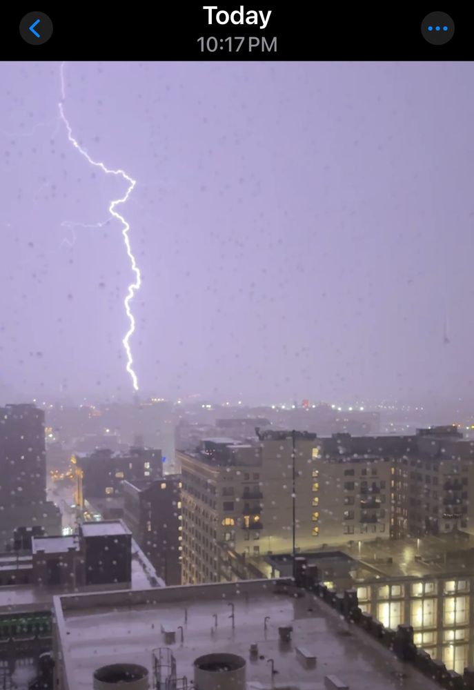 nighttime. cloud to ground vertical lightning strike with small left branch. city below