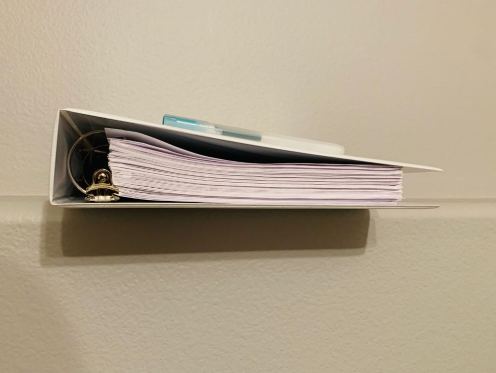 Bottom view of a white binder full of pages, with a green gel pen on top