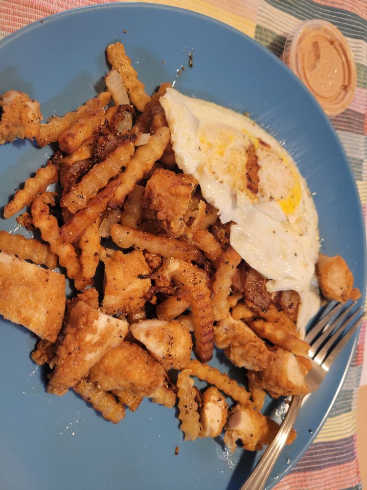 Pile of crisp onions, french fries, and chicken with fried eggs.