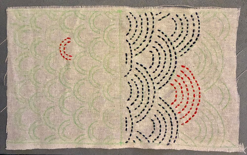 An incomplete sashiko piece in navy and red thread on muslin. The patterns are two sizes of waves, set in opposite directions. 