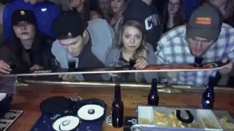 GIF of Four folks at a bar about to drink four shots from a ski. The ski is lifted to their mouths to take the shots in unison. The small blonde girl in the middle can't reach the ski as it is flipped to the taller people, and she is left with dark drink on her face. She chases it with beer anyway.