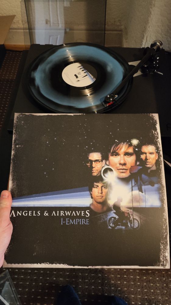 Vinyl cover of a blue stripe across the sky in space with the bands heads on the front and someone on a motorcycle. A blue and black vinyl spinning 