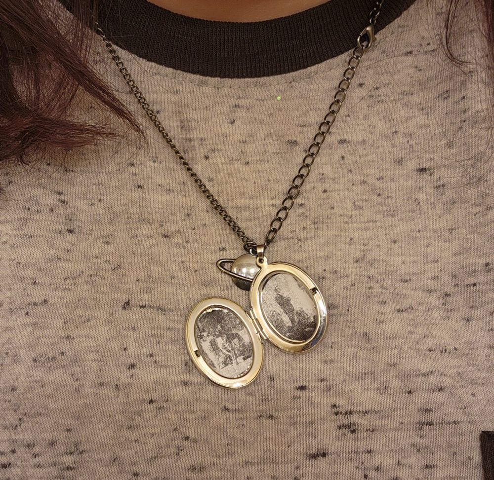 A picture of a person wearing a locket. The pictures are hard to Makeout in the locket but one side is two cats kissing and the other is a groom holding a bouquet 