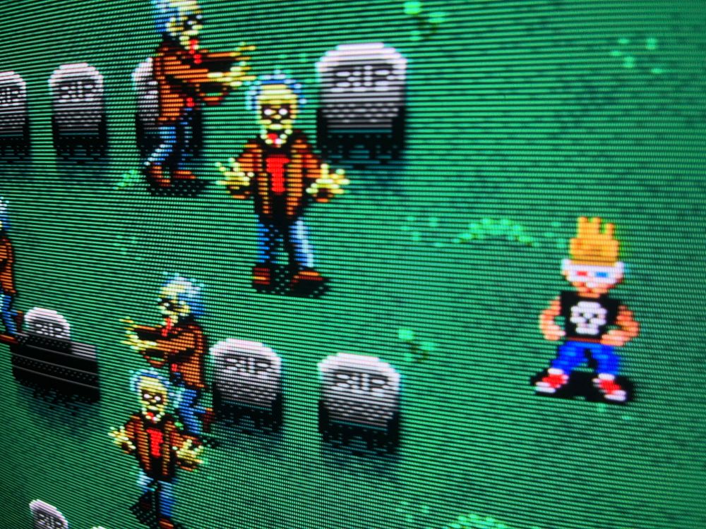 A photograph of Zombies Ate My Neighbors on a CRT. A tubular 90s kid hangs out with Zombies on a graveyard.