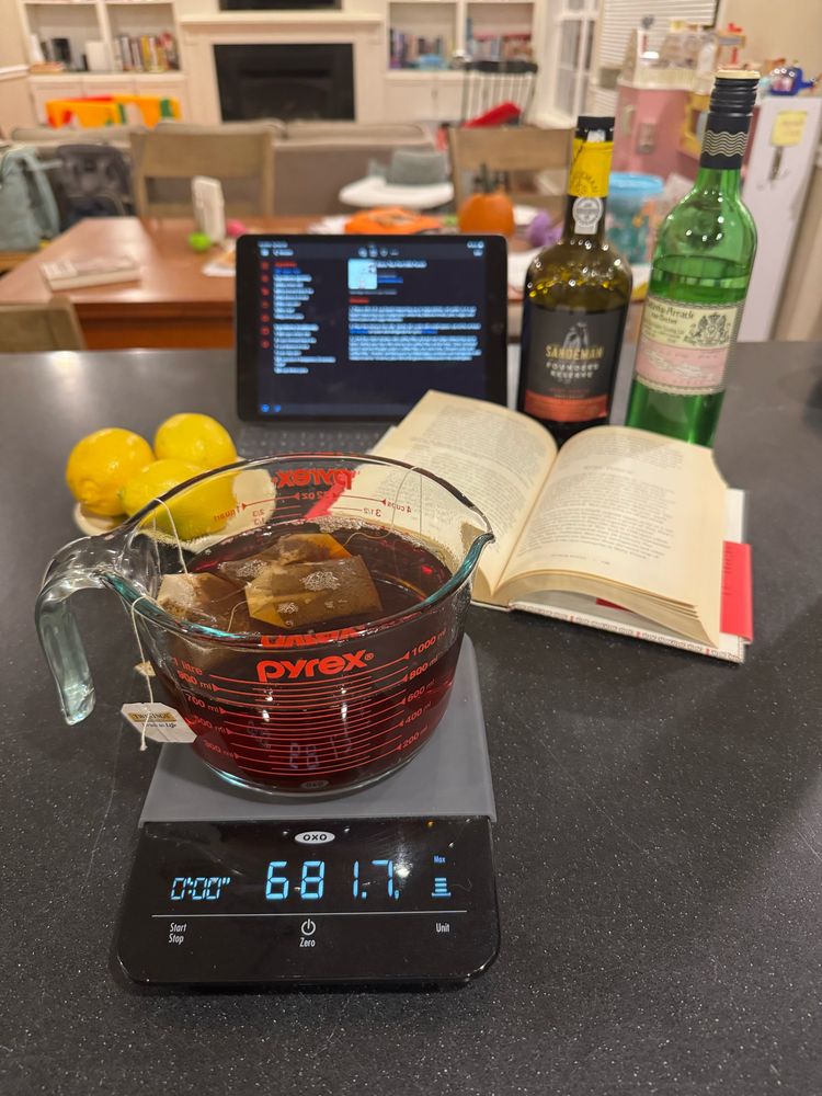 A large bowl of black tea steeping surrounded by the other ingredients for Ruby Milk Punch. 