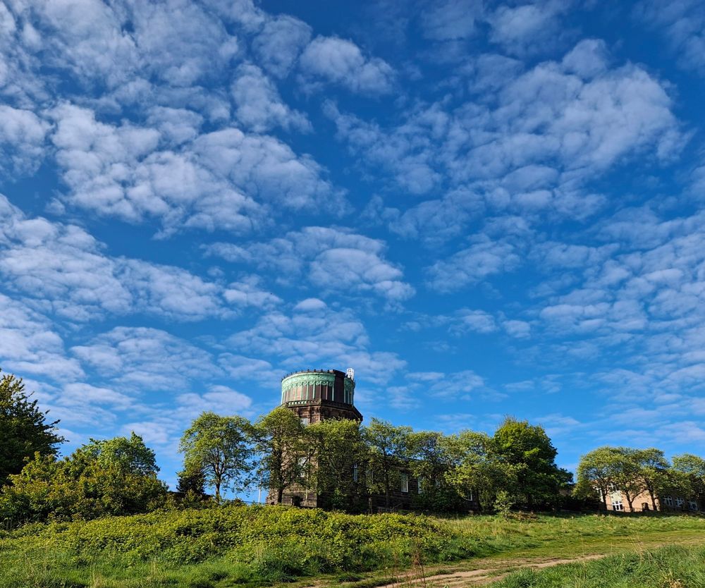 Picture of the dome of the Royal Observatory Edinburgh. Most of the photo is a blue sky with mackerel clouds.