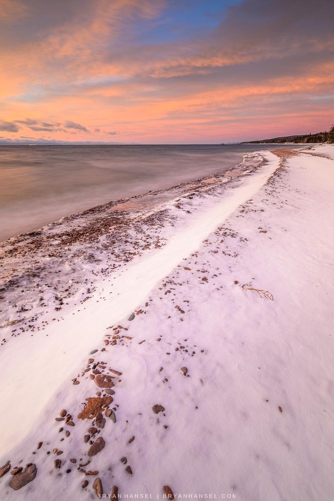 An orange and pink cloud painted sky with a snow beach leading towards it.