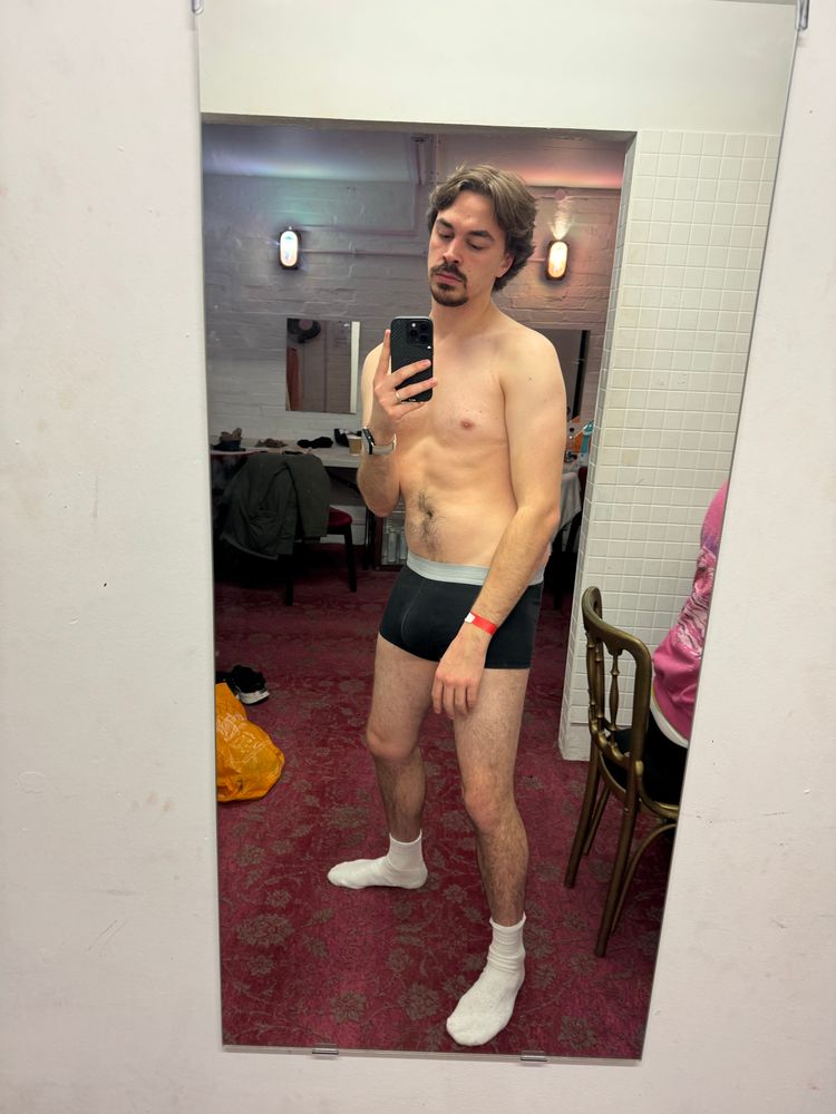 Joseph (with his natural brown hair colour!!!!) stands in his pants and socks in a dressing room. The photo was taken in December 2023, RIP the abs Joseph had back then