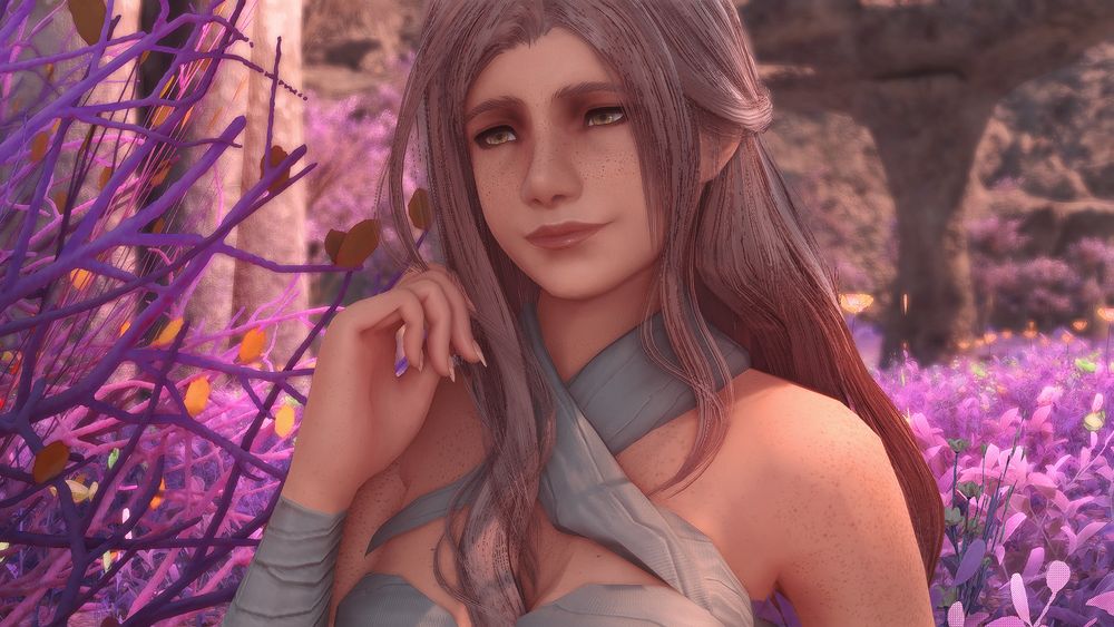 Nayzak, a pale skinned hyur with pastel rose hair, is sitting in a field of violet grass. She is wearing a top made of bandages which wrap around her forearms and chest. Her arms are bare displaying her freckles. Her face is also freckled and a soft smile adorns it. Her hand is raised by her face, touching her hair.