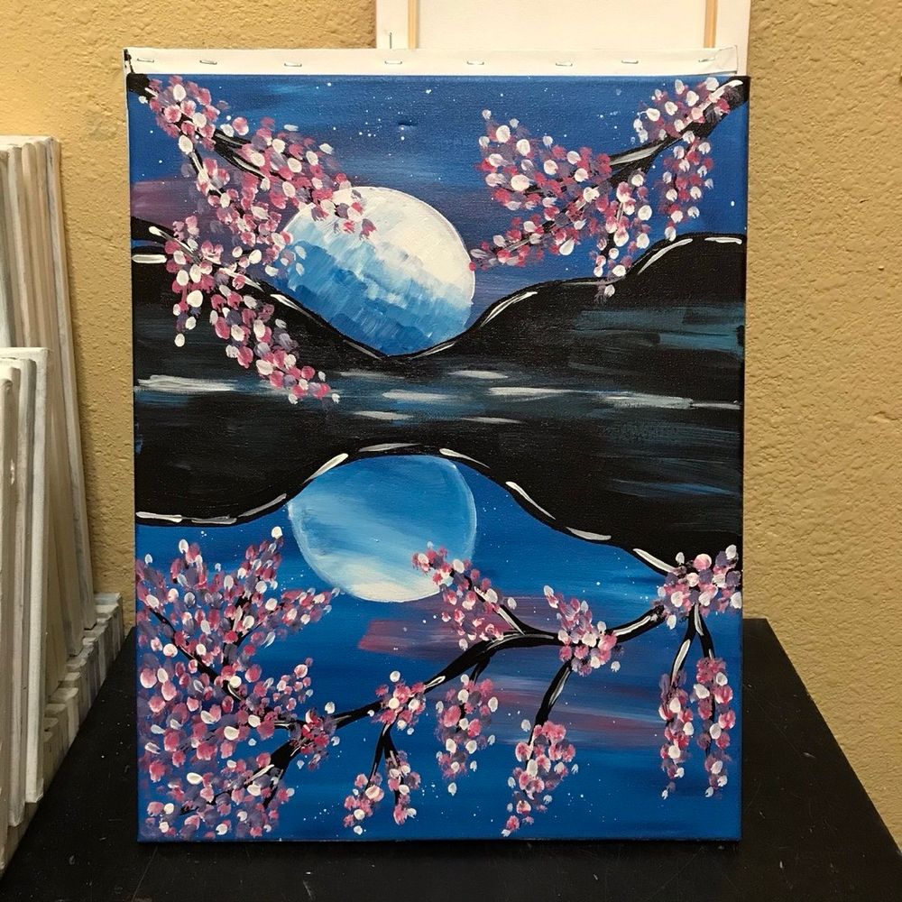 A painting of a full moon above mountains and cherry blossoms that has a reflection in the water below.