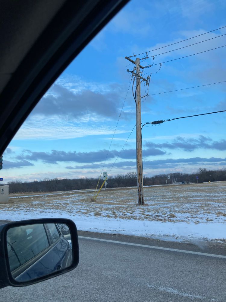 A picture taken out of a car window. There is a light dusting of snow and the picture shows blue skies, clouds, and an electric pole.