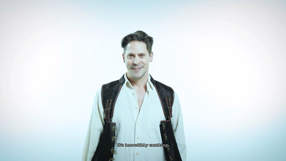 Neil Newbon dressed in a white button down and black vest, smiling at the camera

Text: "It's incredibly exciting."