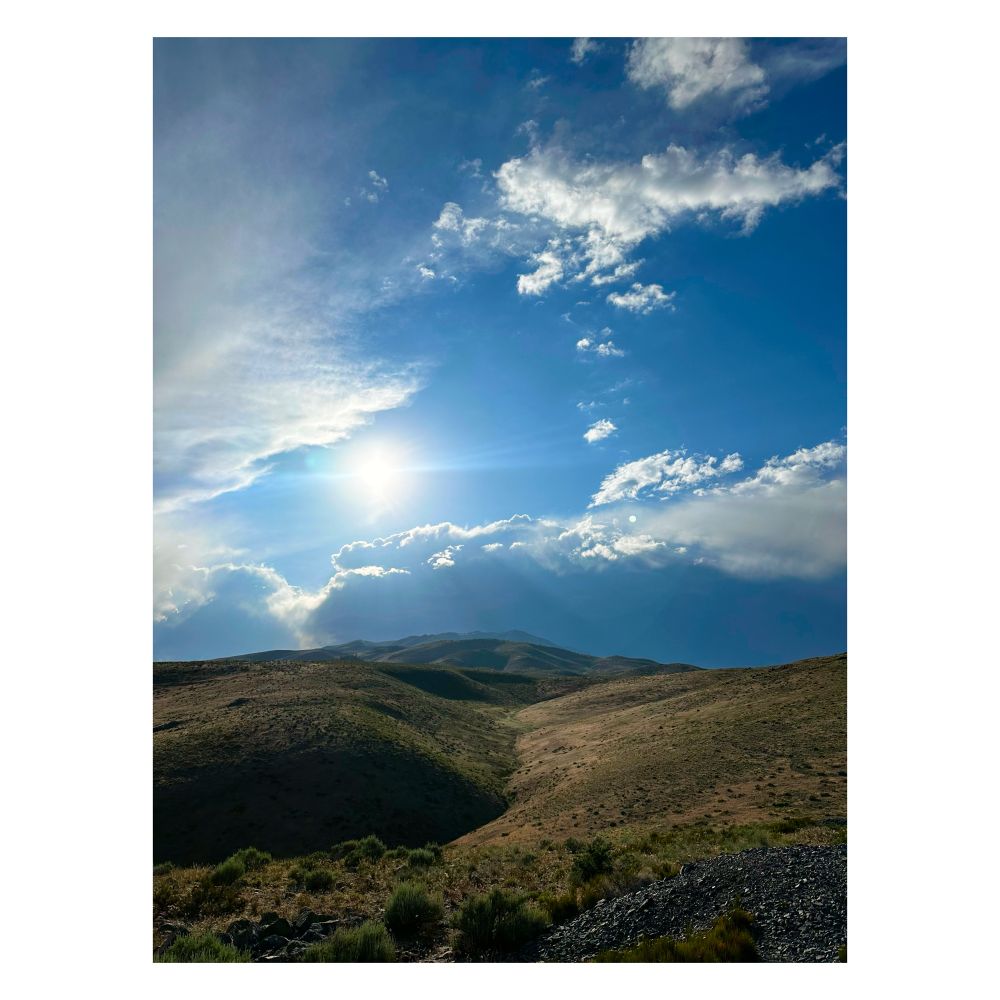 View toward the top of a mountain where the Sun surrounded by a few clouds seemingly awaits.