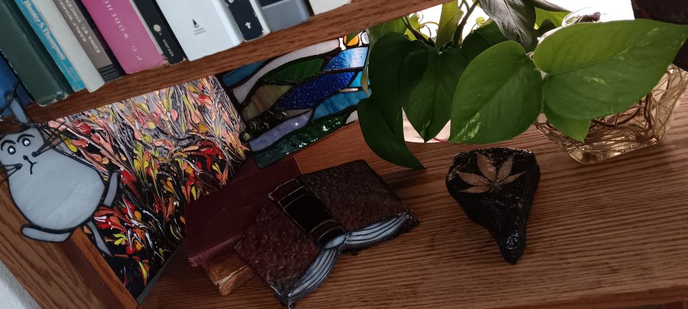 Art shelve on a bookcase. Gifted art, stained glass, painted rock shaped like nevada with a cannabis leaf shelacked on. Plant starters. Looks cool i think