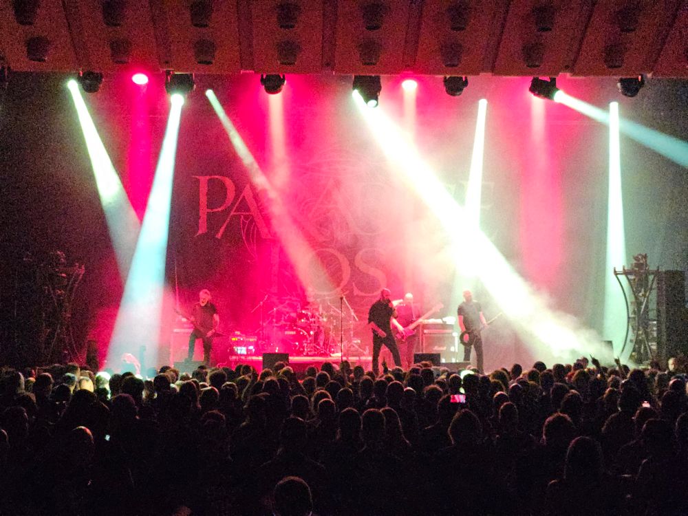 Bilde av metalband på scenen, med rødt bakgrunnslys, og hvite lyskastere.