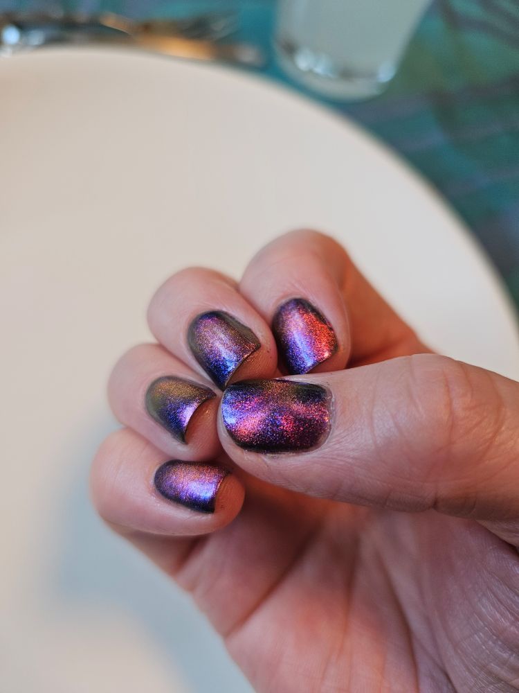 Høyrehånda mi, med neglene synlig. Jeg har på en blålilla neglelakk med fuksiafarget til rødlig magnetisk pigment oppi, slik at dette flyttes på med magnet og den andre fargen også kommer frem. På tommelneglen er det magnetisert som et kryss. På de andre neglene er det forsøkt å magnetisere på diagonalen.