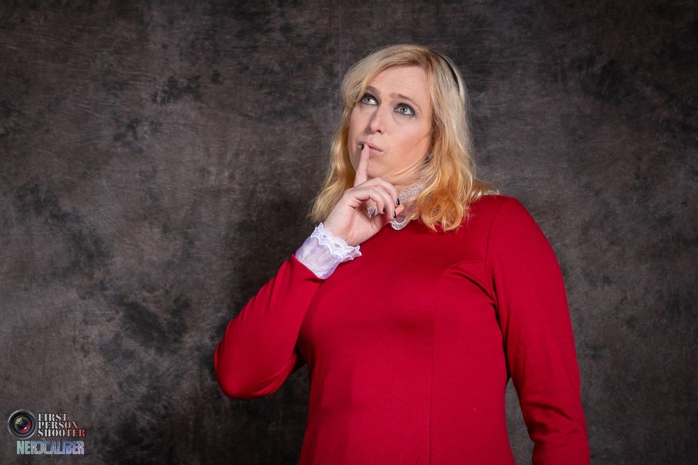 A cosplayer is dressed as Sabrina from the Netflix series The Chilling Adventures of Sabrina. She holds a finger to her mouth in a contemplative gesture.