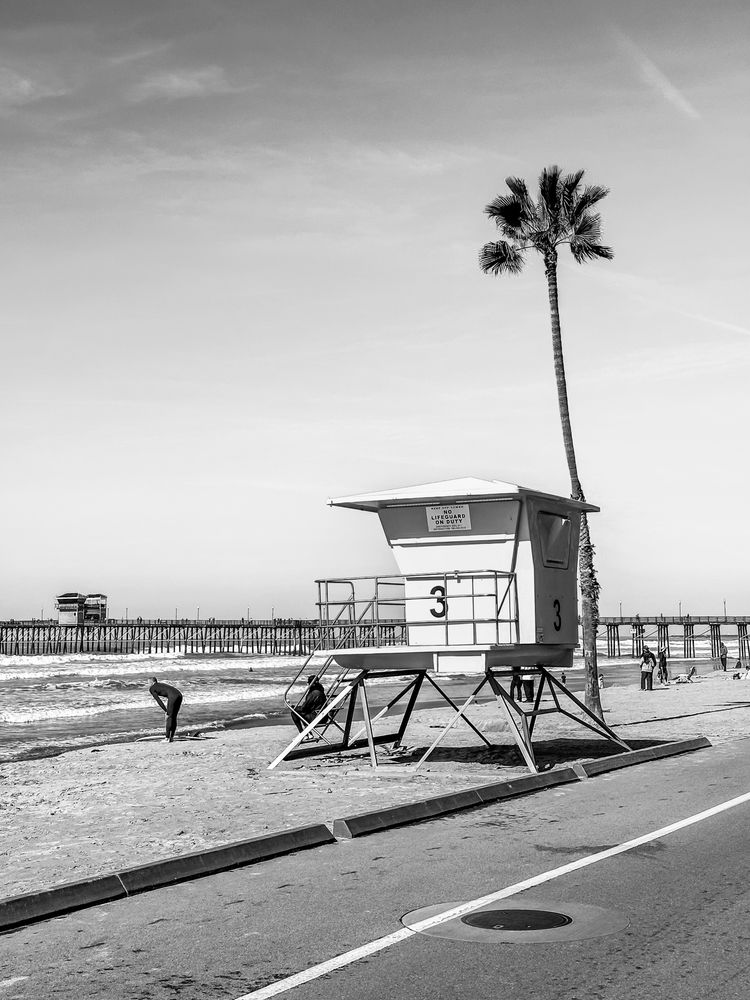 black & white pic of a lifeguard tower and a pier in the background 