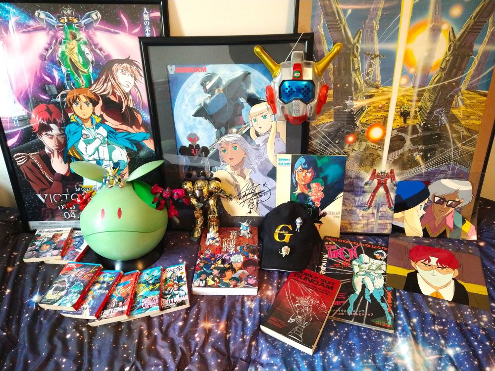 An assortment of various Tomino-related goods!
Left: Victory Gundam Memorial DVD boxset poster, F91 novels, 1/1 Haro with MS in Pocket red Zolo and Contio figures poking out from inside it and a SD Converge V2 atop its head, Victory novels
Center: Turn A Gundam poster signed by Tomino himself with a Ideon kid's mask hanging on its top corner, World of Yoshiyuki Tomino Retrospective book with 1/100 Gold SUMO, SD Converge Turn A and G-Self on top of it, the "G-Reco" baseball cap with SD Mask and Raraiya keychains, Mobile Suit Gundam novels omnibus
Right: Mitsuki Nakamura Space Runaway Ideon poster, A Contact & Be Invoked film booklet, Ideon Animation Cel Collection Part 11 book, cels of Harry & Dianna from ep 22 of Turn A and of Cronicle from ep 1 of Victory