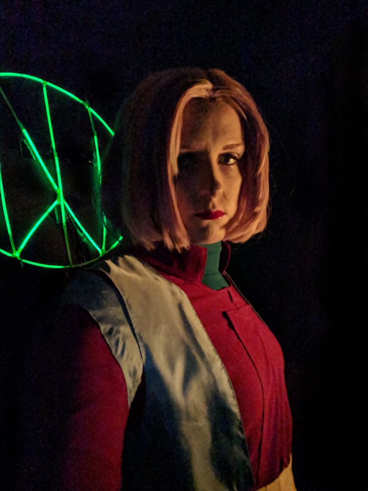 2017 photo of me cosplaying Sheryl Formosa, with an Ide Gauge fashioned out of glowsticks and duct tape shown behind me