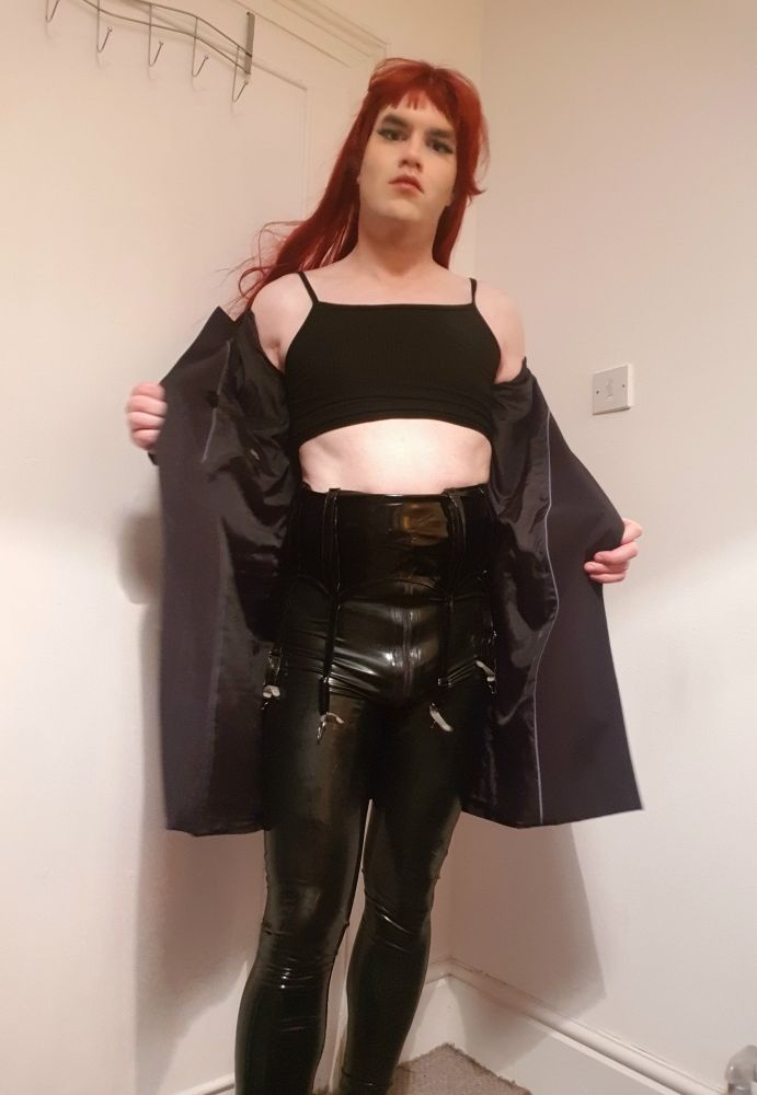 Lexei, dressed in latex pants, boots and a black top removes her black coat revealing her outfit.