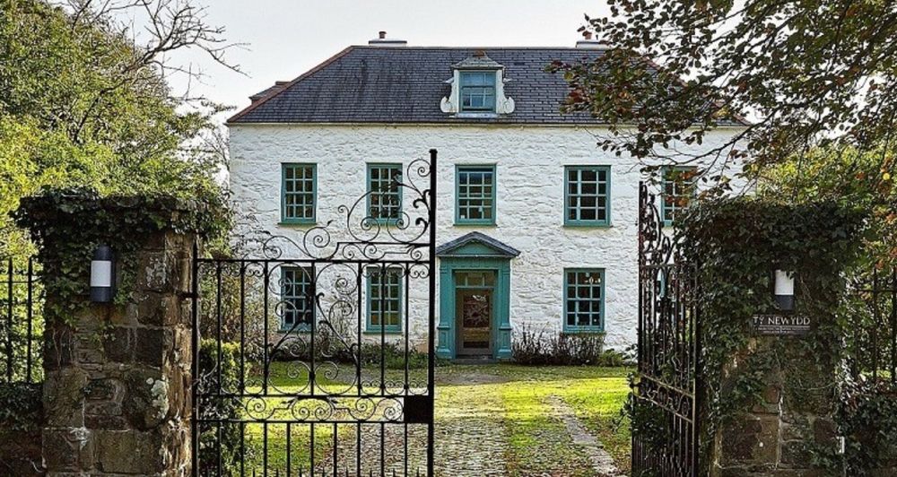 Picture of white double fronted house set in gardens with iron gates 