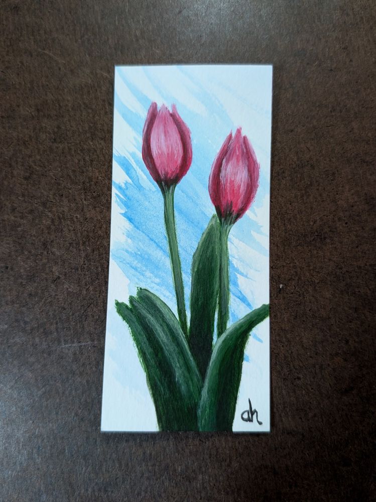 One vertically painted bookmark pictured. The bookmark shows two small closed tulips, not yet fully bloomed. The tulips are are dark pink to red color. There's a splash of blue coloring the background. 