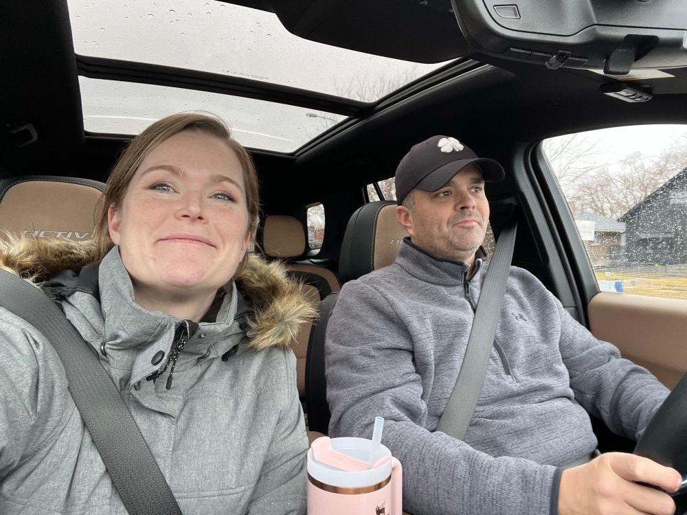Selfie of woman and man in gray coats riding in a car. 
