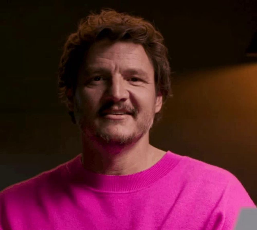 a man with a beard wearing a pink sweater is smiling .