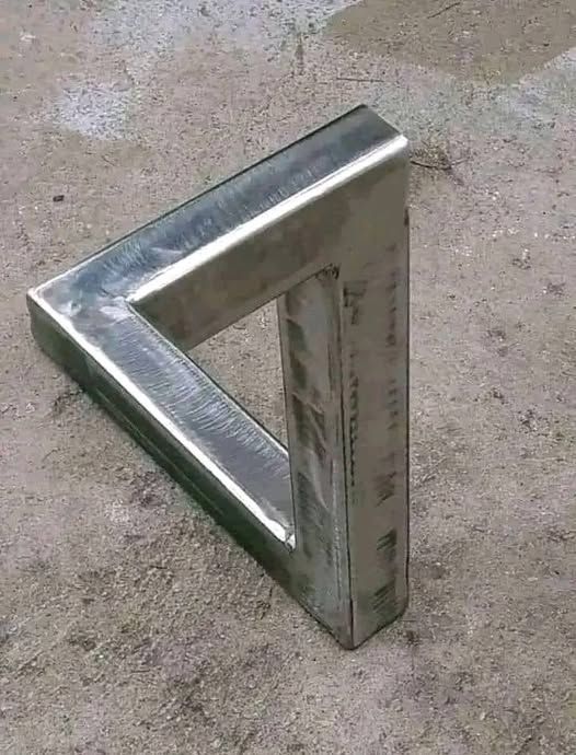 Objet en métal formant un triangle de Penrose, créant une illusion d'optique de triangle impossible, posé sur le sol.