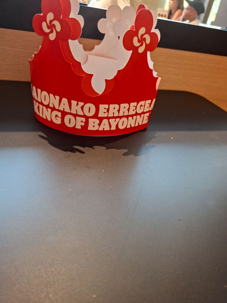 A paper burger king crown with text in Basque and a basque cross sits on a table.