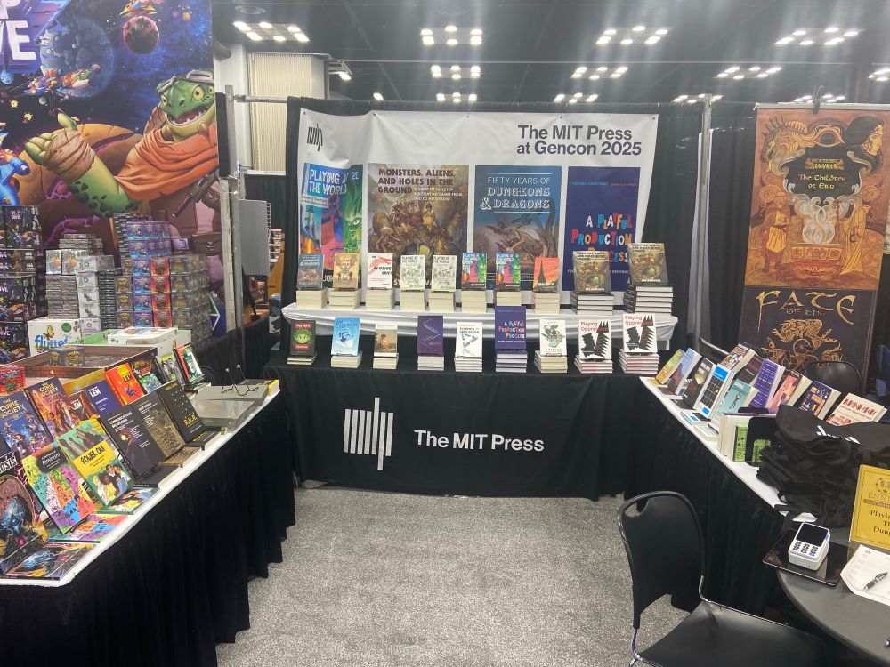 The MIT Press booth at GenCon 2025. The picture shows stacks of amazing books for sale!