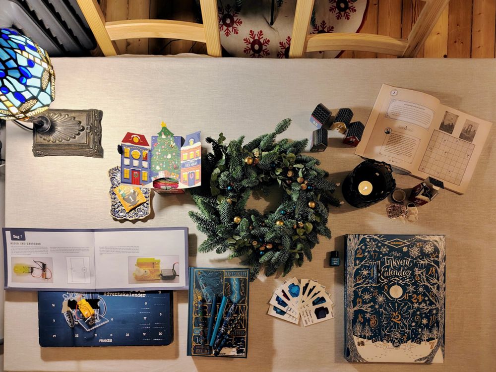 Inkvent packaging on a table, surrounded by a wreath, a lit candle, and other Advent calendars.