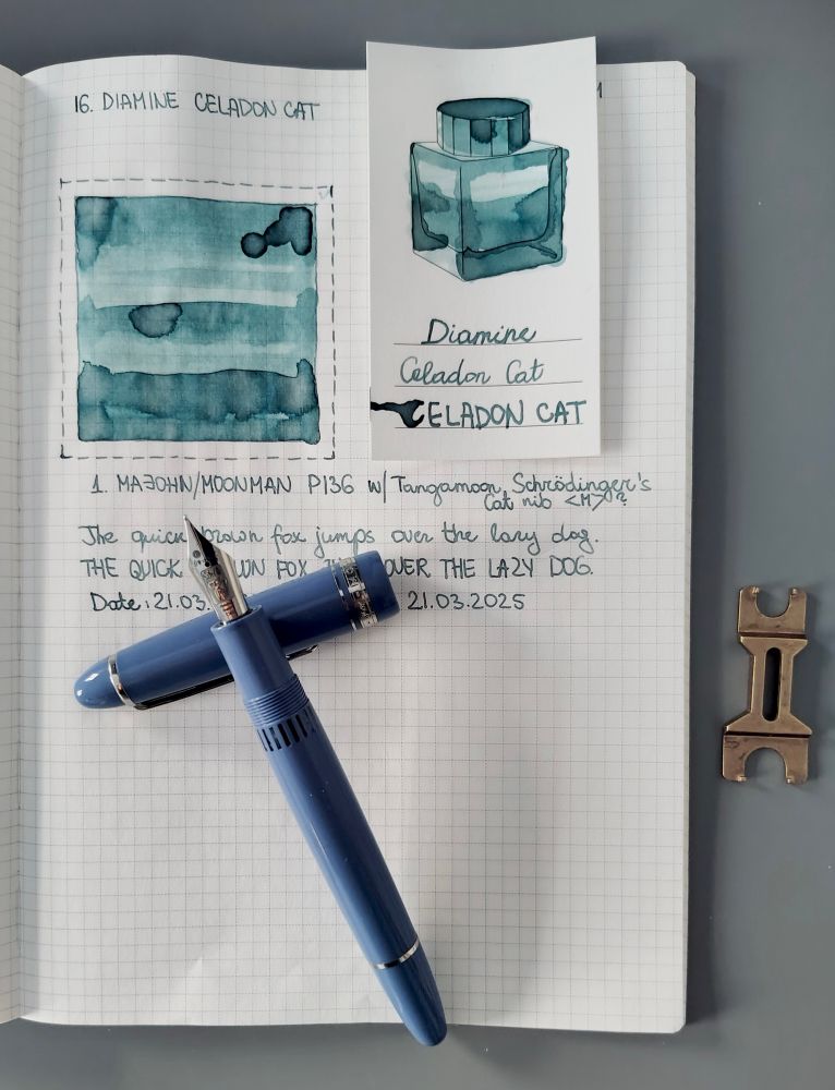 Open notebook with blue-greenish ink swatch and handwritten text. A light blue-violet fountain pen with Schrödinger’s Cat nib lies across the notebook. A small metal wrench is beside it.
