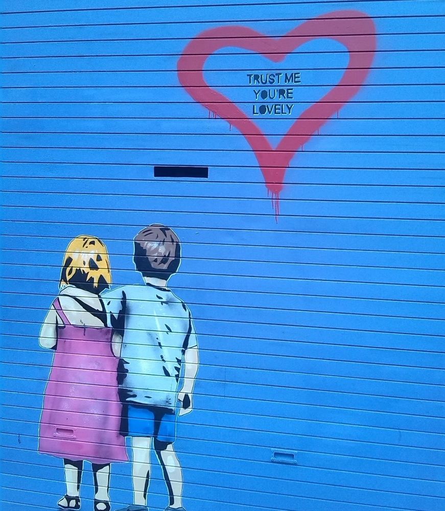 Street Art, Dublin. The words in the heart say 'Trust me you're lovely' and 2 children (a girl & a boy) are seen from the back, with the little boy placing his arm protectively around the little girl.