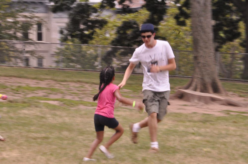 Photograph of a youth playing tag with a child at a summer camp for urban youth.