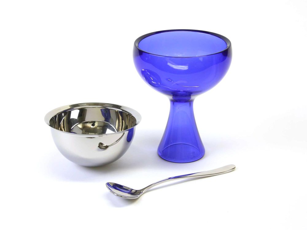 On the right is the outer bowl made of blue translucent acrylic, it has a long tapered stem and a wide opening.  On the left is the steel liner dish, and at the front a steel heart shaped spoon with a long handle.