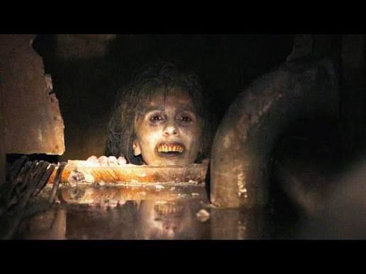 The corpse mom from Caveat (2020) popping up from below to smile her dead smile at you. Her hands, holding her up so she can rest her chin on the secret crawl space ledge, are just visible.