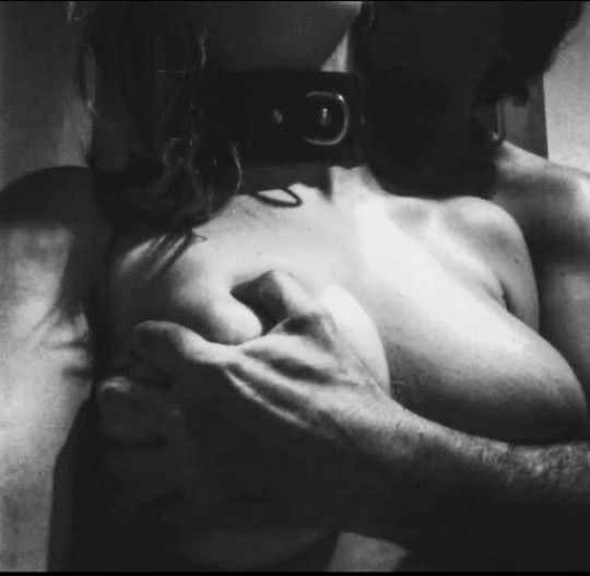 Collared femme, arms behind her, man's hand reaching around from behind to grip her breast