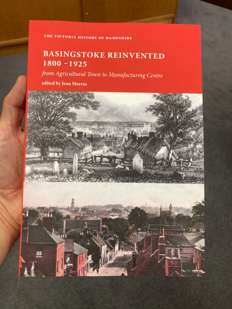 Front cover of a book, entitled 'Basingstoke Reinvented, 1800-1925, from Agricultural Town to Manufacturing Centre', edited by Jean Morrin.

The title is white on a red band occupying the top third of the cover. Beneath are two views if the town from the same spot. The top (a black/white engraving), shows trees and thatched cottages. The lower image, a hand tinted photograph shows the 19th century streets that replaced the cottages, c. 1920.