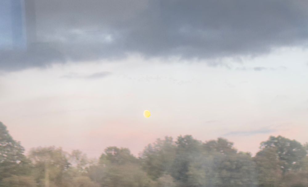 Heavy band of menacing cloud hangs over a pink landscape and yellow moon
