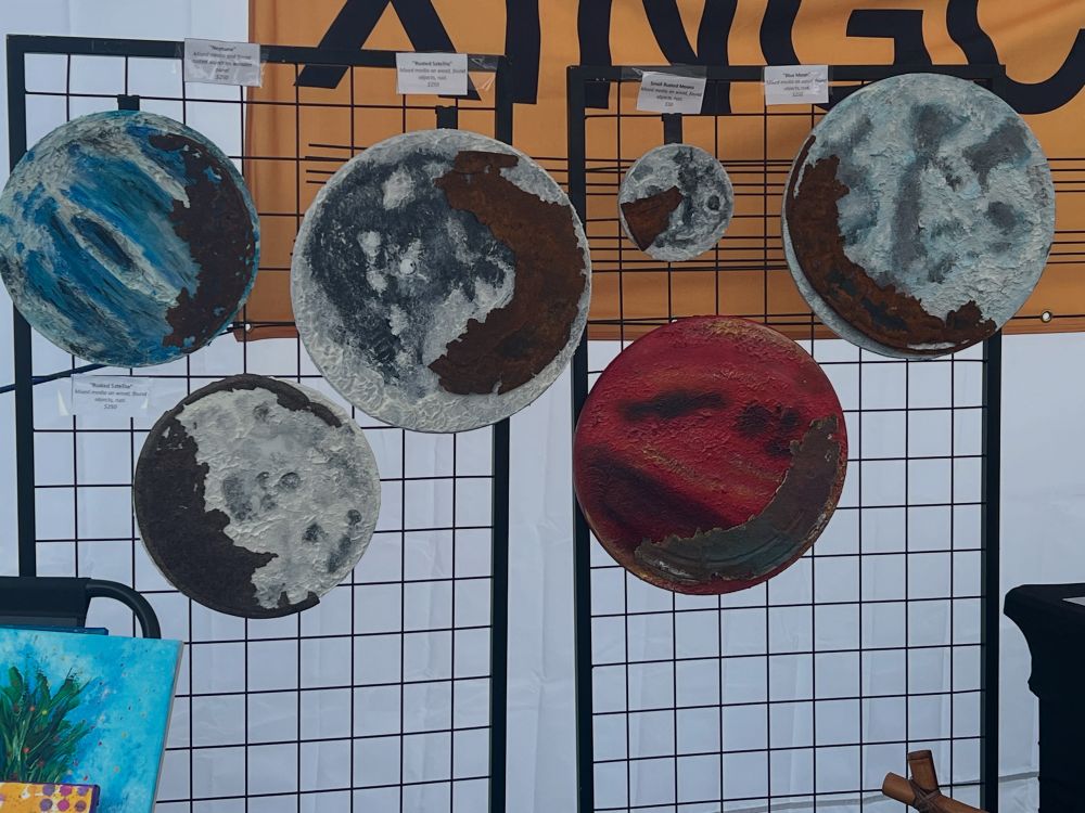 A display grid wall full of abstract moon paintings that feature rust. 