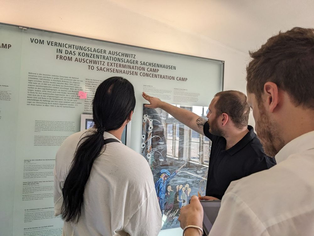 Drei Teilnehmende des Interventionsprojekts "Wir intervenieren" stehen vor einem Ausstellungselement in der Ausstellung über die Sinti* und Roma* im KZ Sachsenhausen. 