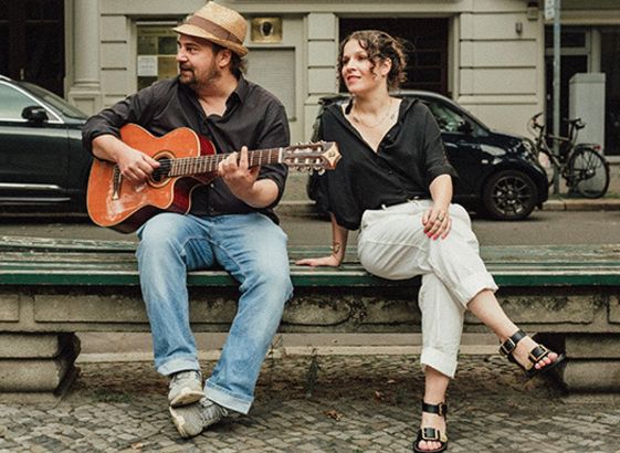 Marcel Weller mit Gitarre und Anne Helm sitzen auf einer Parkbank. Das Foto soll ihr gemeinsames Konzert in Berlin am 30.09. bewerben.