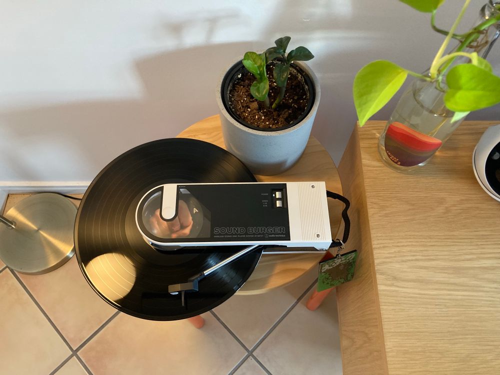 Top down view of a record being played on an audiotechnica sound burger, an 80s throwback mini turntable where the record sticks all the way out like a buzzsaw blade