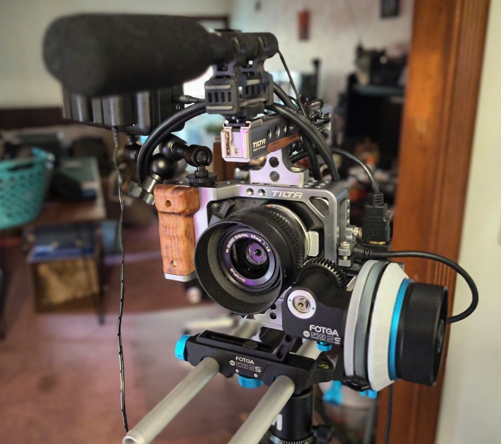 A blackmagic pocket cinema camera rig, consisting of the camera, a follow focus system, a microphone, a wood furniture cage for the camera, and an external recording system.