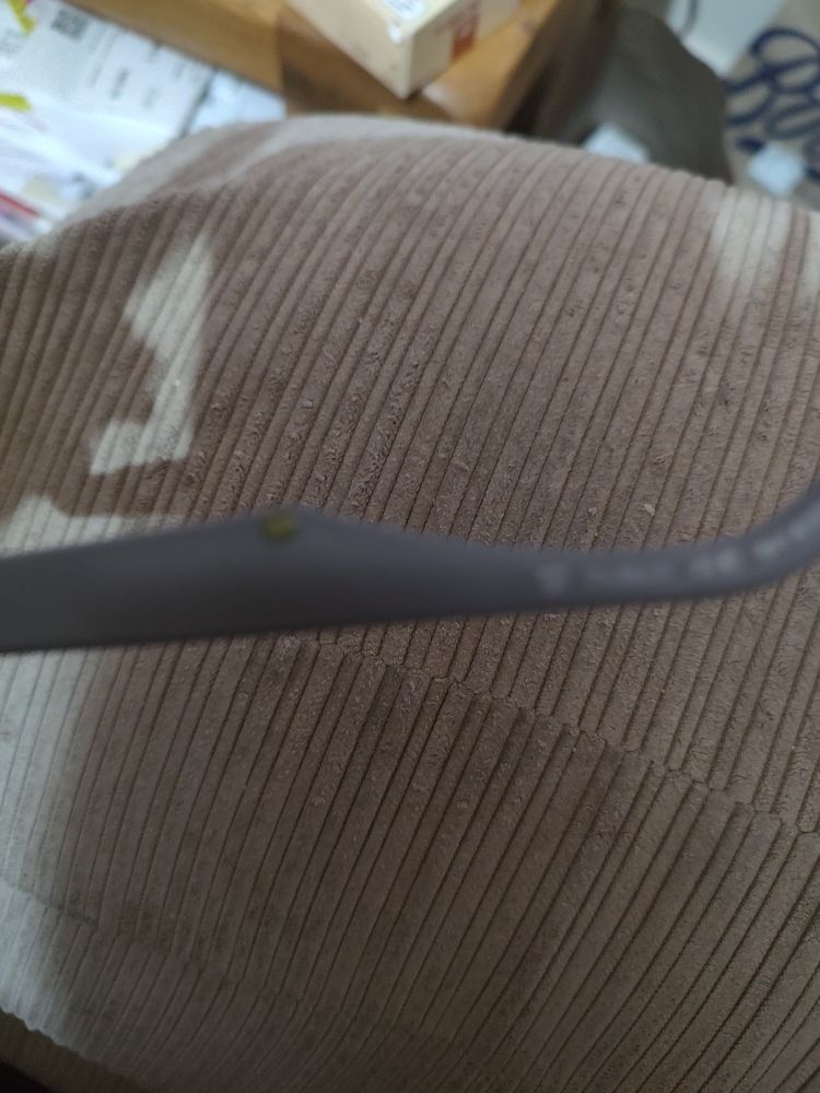 Arm of a pair of glasses against a background of a sofa. There's a drop of greeny yellow liquid visible on part of the arm.
