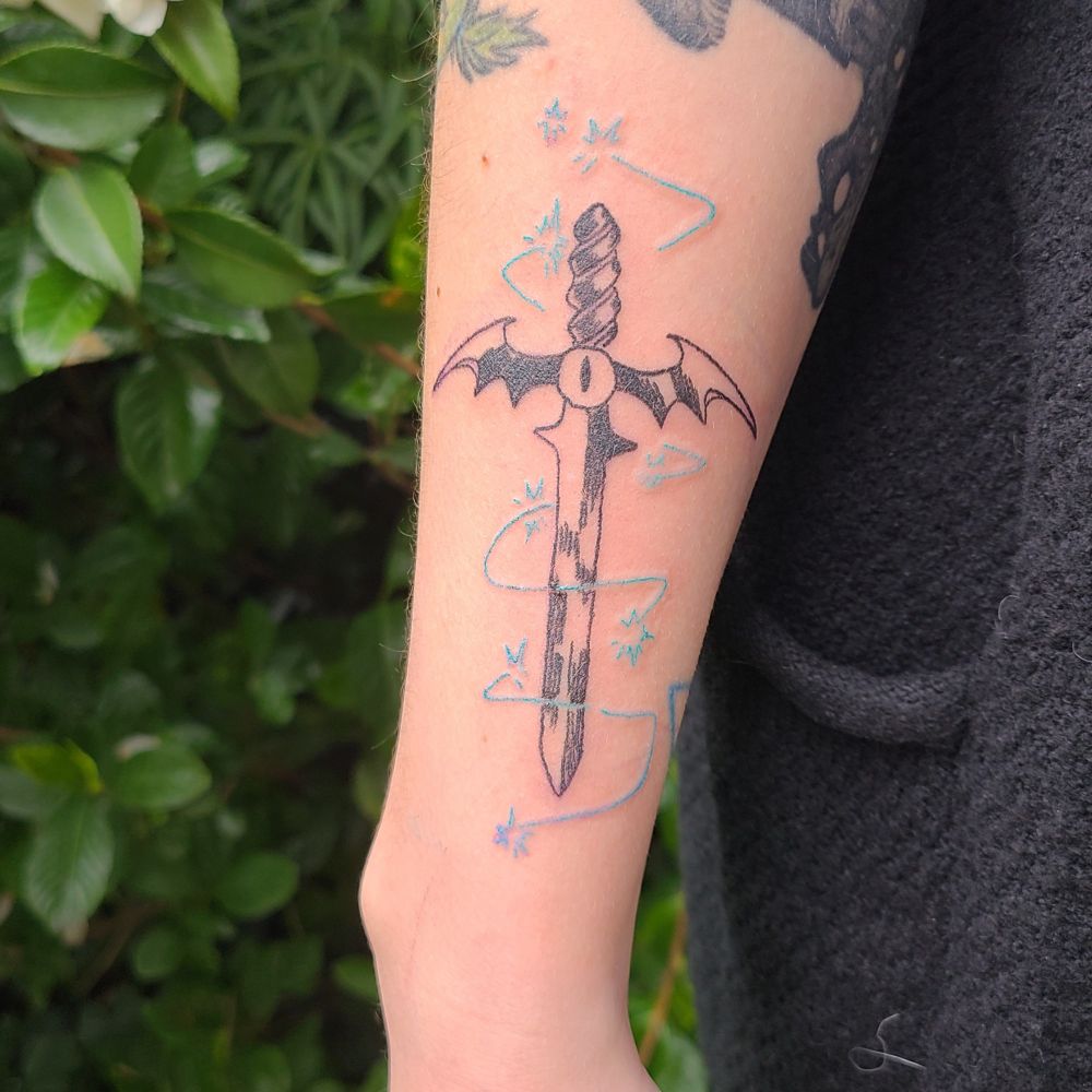 demonic cartoon sword tattoo on a client's forearm.