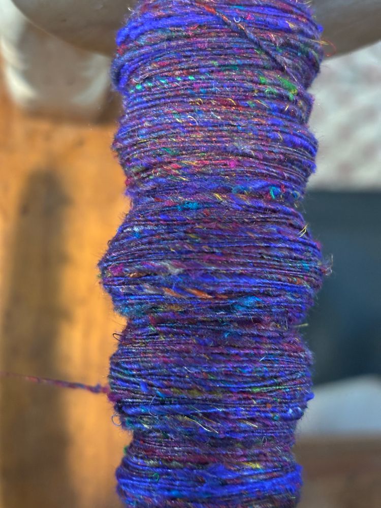 A bobbin (still on the spinning wheel) of purple yarn with colorful bits